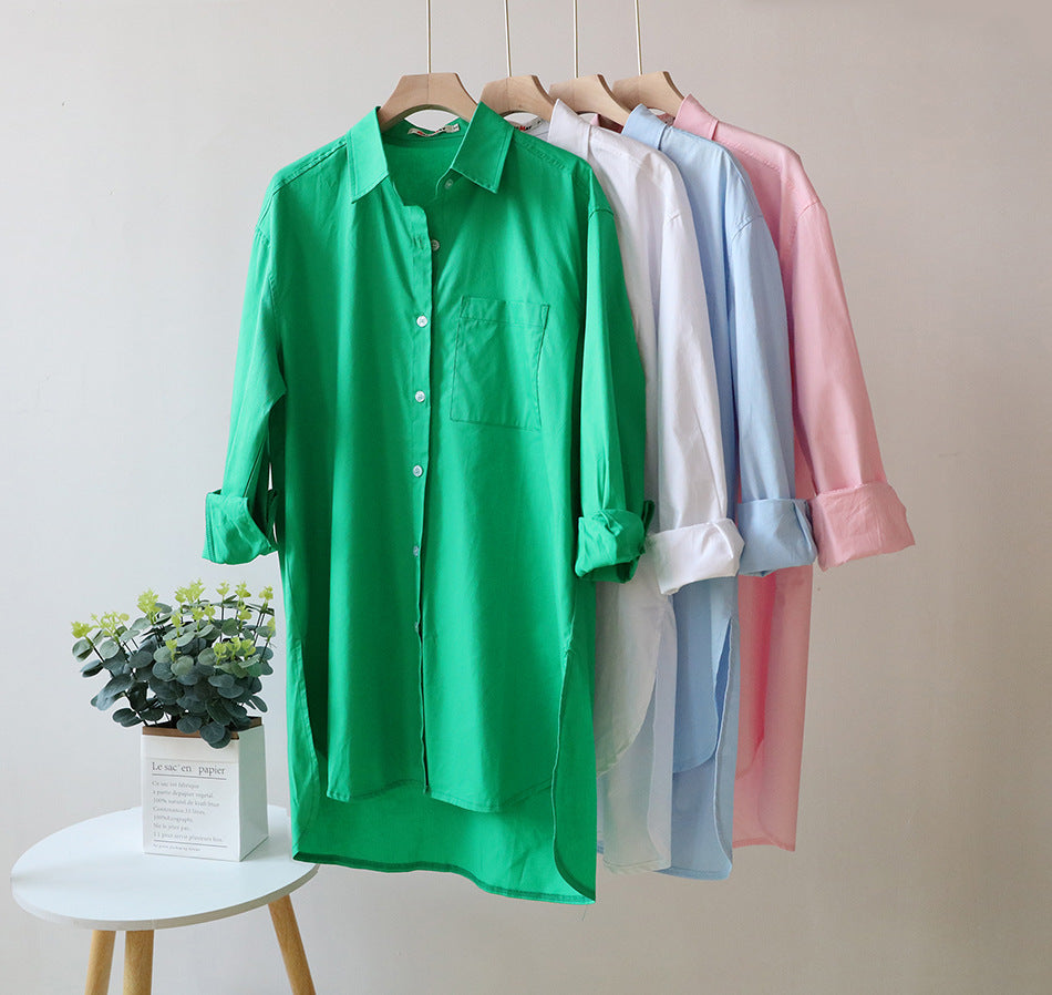 Green, white, light blue, and pink shirts hanging on a rack with a small plant on a table.
