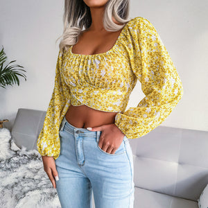 Woman wearing a yellow floral blouse and light blue jeans in a modern living room.