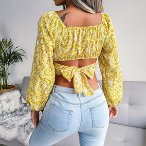 Person wearing a yellow floral top with a tied front and light blue jeans in an indoor setting.