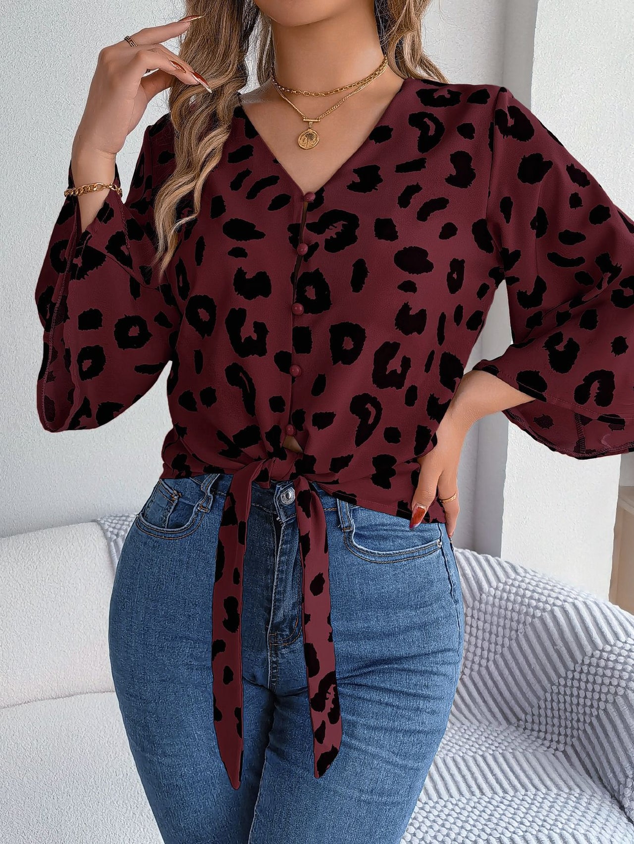 Person wearing a burgundy blouse with black leopard print and blue jeans indoors.