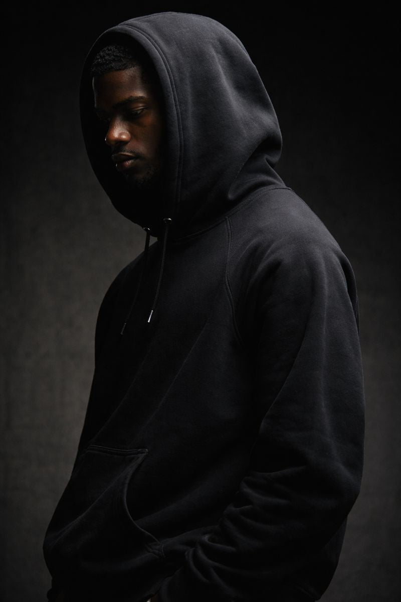 Black premium streetwear hoodie with gold chest crest and symbolic back graphic worn by a Black male model in a minimalist luxury photoshoot.