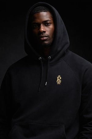Black premium streetwear hoodie with gold chest crest and symbolic back graphic worn by a Black male model in a minimalist luxury photoshoot.